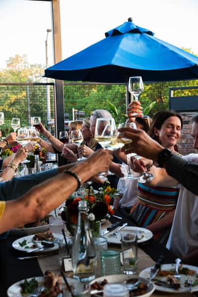 People cheersing glasses under a blue umbrella on Farm Bar Ravenswood's rooftop