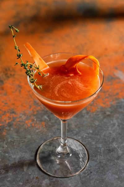 the Wascally Wabbit. Orange liquid in a martini glass with an orange peel and other garnishes