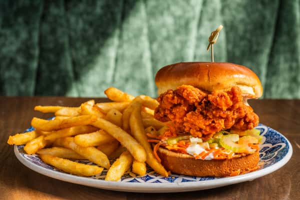 buffalo chicken sandwich sits on plate next to fries
