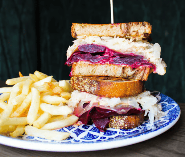 Sandwich with purple beets on a blue plate sitting in front of a wall of green velvet