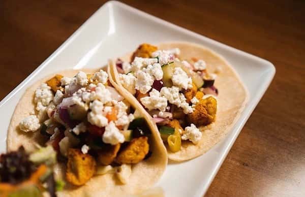 Street tacos with a variety of toppings, cojita cheese, on a long flight plate.