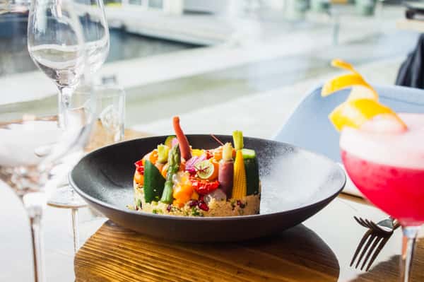Colorful seasonal vegetable salad with fresh market produce, edible flowers and vibrant ingredients served in an elegant waterfront dining setting.