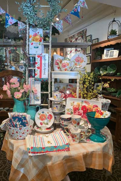 Round table with a yellow checkered tablecloth decorated with flowers in various sizes and a variety of other floral decorated dishware