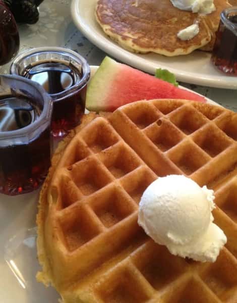 Belgian waffle with butter and a side of maple syrup and a slice of watermelon