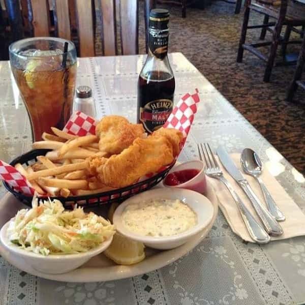 Fish and chips basket with side of coleslaw a glass of iced tea and bottle of malt vinegar