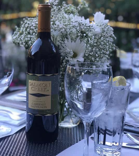 Bottle of Salmon Creek next to glasses and white flowers
