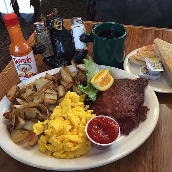 Scrambled egg entree with breakfast poatatoes and ketchup ona table with hot sauce and a cup of coffee