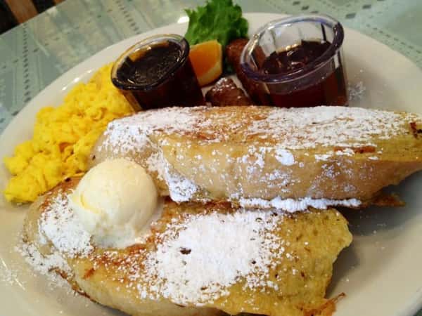 French toast with powdered sugar and scrambled eggs and maple syrup on the side