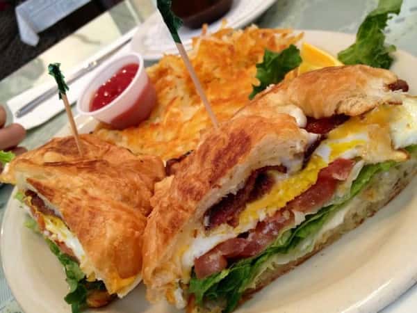 Egg sandwich on a croissant with bacon lettuce tomato and side of hashbrowns