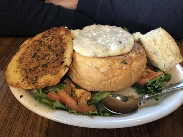 Clam chowder soup in a bread bowl over lettuce and tomato on a plate