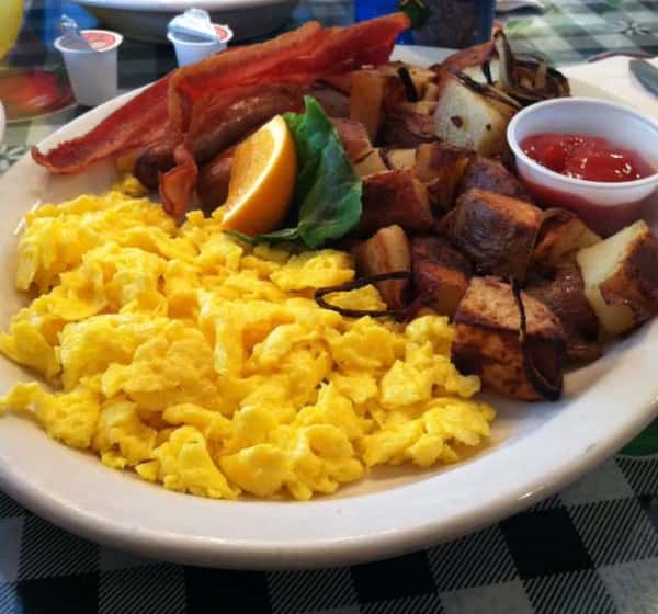 Scrambled eggs on a plate with breakfast potatoes bacon and a side of ketchup