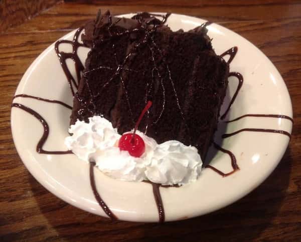 Slice of chocolate cake with whipped cream and a cherry