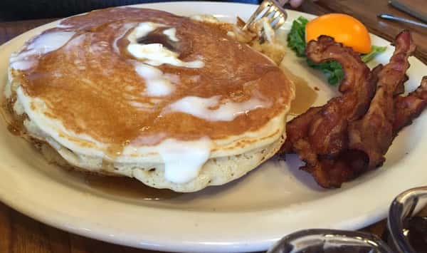Stack of pancakes on a plate with bacon and orange slice
