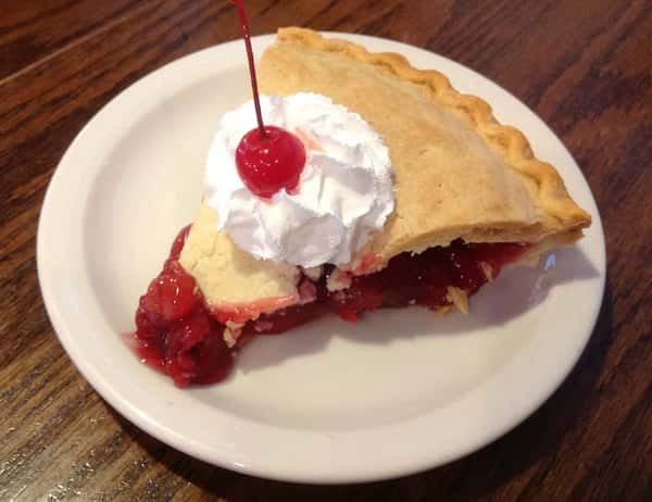Slice of cherry pie with whipped cream and a cherry on top