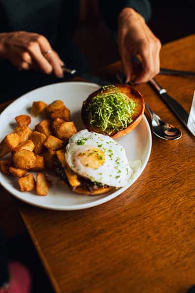 Burger topped with a fried egg with a side of diced potatoes