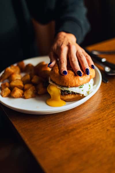 Woman's hand pressing down on a burger with a sunnyside egg oozing out