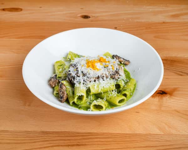 Creamy pasta topped with shaved cheese and herbs, served in a white bowl on a rustic wooden table.