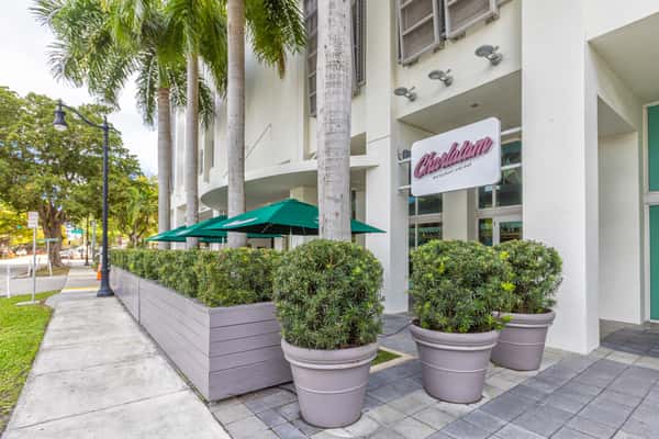 Restaurant entrance exterior with landscaped planters, outdoor walkway, and welcoming storefront.