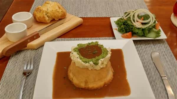 Pot pie topped with sauce or gravy, garlic mashed potatoes, smashed green peas