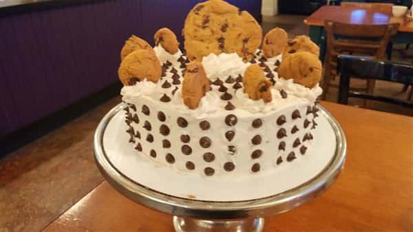 White frosting cake topped with chocolate chip cookies and drops of chocolate