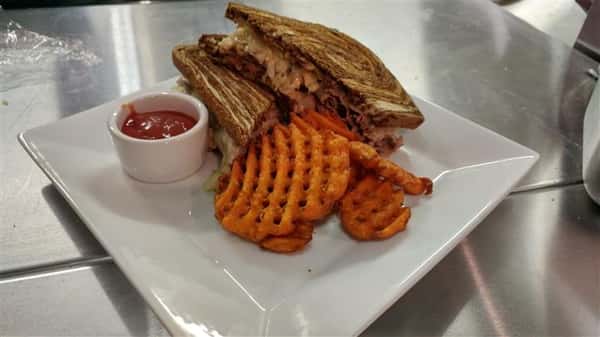 Classic reuben sandwich halved and served with sweet fries and ketchup