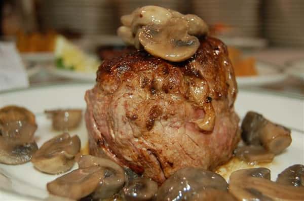 Cooked steak on a plate with mushroom sauce on top.