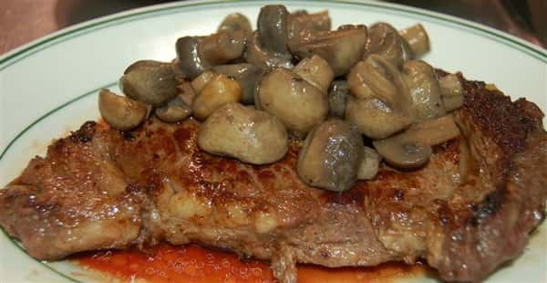 Cooked steak on a plate with mushroom sauce on top.