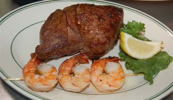 New York Strip steak on a plate with grilled shrimp and lemon wedge on the side.