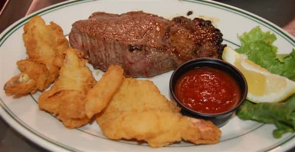 New York Strip Steak with fried shrimp on the side and cocktail sauce.