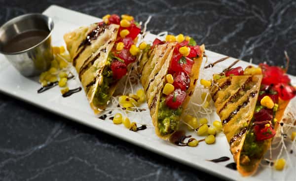 sushi tacos with avocado, tuna, corn, cilantro and a brown sauce in a crispy tortilla served with more sauce on the side