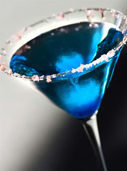 blue cocktail being poured into a glass with candy on the rim