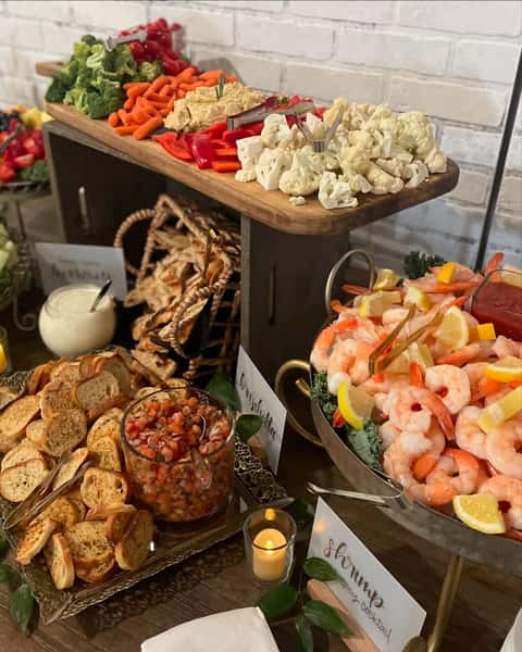 A colorful catering display with fresh vegetables like broccoli and carrots, a shrimp cocktail with lemon, and a bowl of salsa, ideal for weddings and corporate events.