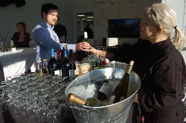 A bartender hands a drink to a guest at a stylish event, surrounded by a variety of wines and spirits in a chilled bucket