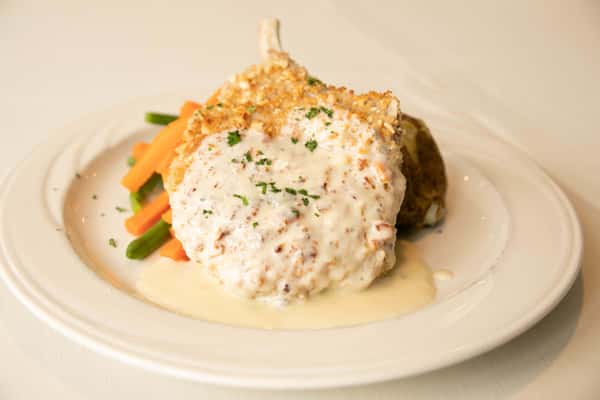 A beautifully plated entrée featuring a tender piece of protein topped with a rich, creamy sauce and a generous portion of fluffy white rice. It's garnished with finely chopped herbs and crispy bits for added texture, accompanied by a side of fresh, colorful vegetables like carrots and green beans, creating a warm and comforting, homestyle presentation.