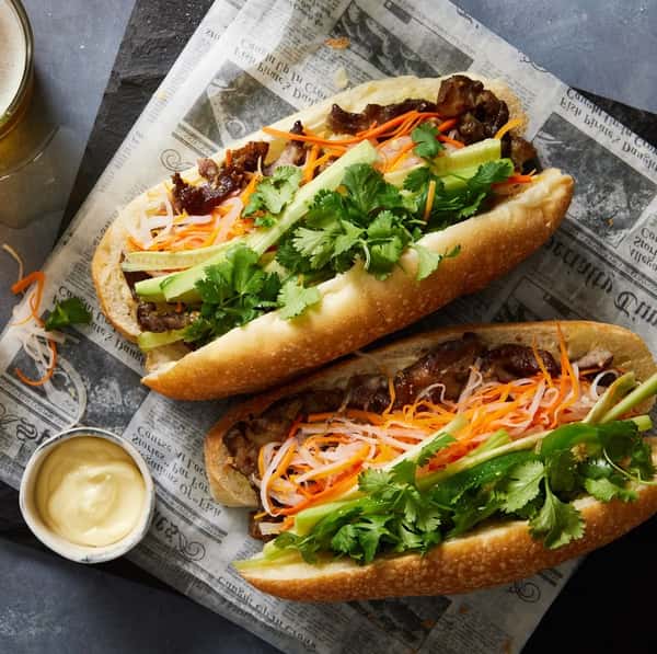 Two crispy rolls filled with meat and sliced carrots, along with greens and a side of sauce