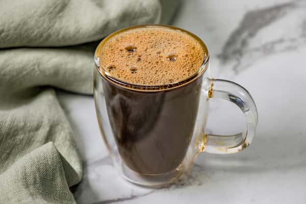 Glass mug filled with freshly brewed black coffee, resting on a marble surface beside a folded green cloth.