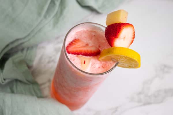 A refreshing strawberry smoothie garnished with a strawberry, pineapple, and lemon slice on the rim of the glass.