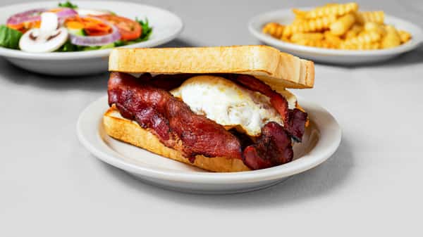 A hearty bacon, egg, and toast sandwich served with a side of crinkle-cut fries and a fresh salad of mixed vegetables.