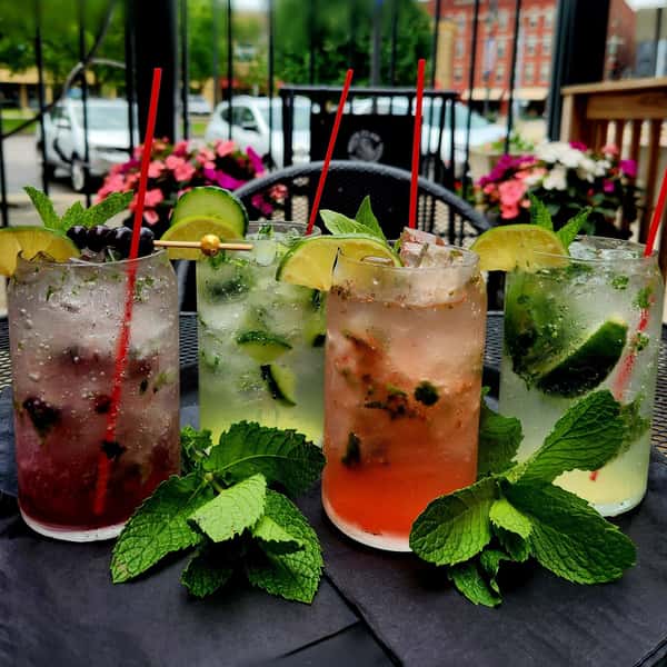Colorful mojito cocktails garnished with mint and lime, served outdoors on a black table with fresh mint sprigs and floral decor.