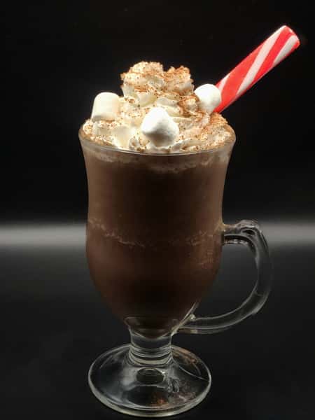 Hot chocolate topped with whipped cream, marshmallows, and cocoa powder, served with a red and white striped candy cane straw.