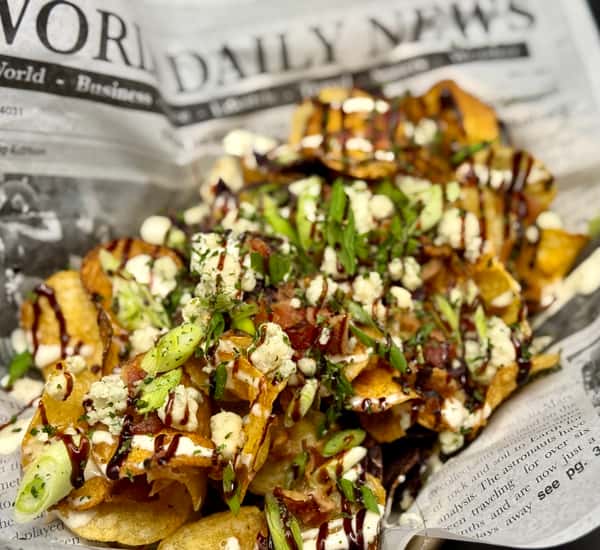 Loaded potato chips topped with green onions, bacon, blue cheese crumbles, and drizzle sauces, served on newspaper-style paper.