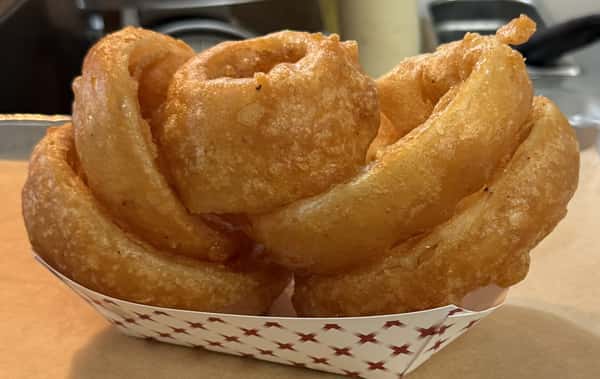 Crispy, golden onion rings are piled high in a paper container at Main Street Eats.