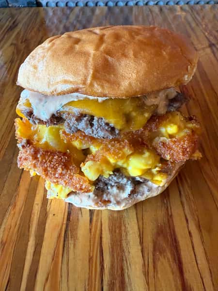 A cheeseburger with fried mac and cheese sits on a wooden surface at Main Street Eats.