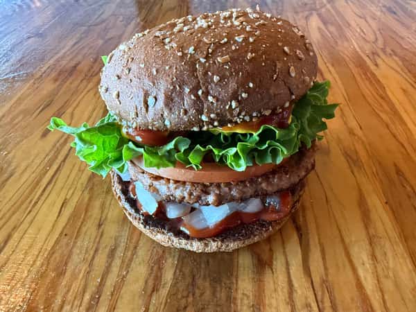 A double-patty burger topped with lettuce, tomato, and onions sits on a wooden surface at Main Street Eats.