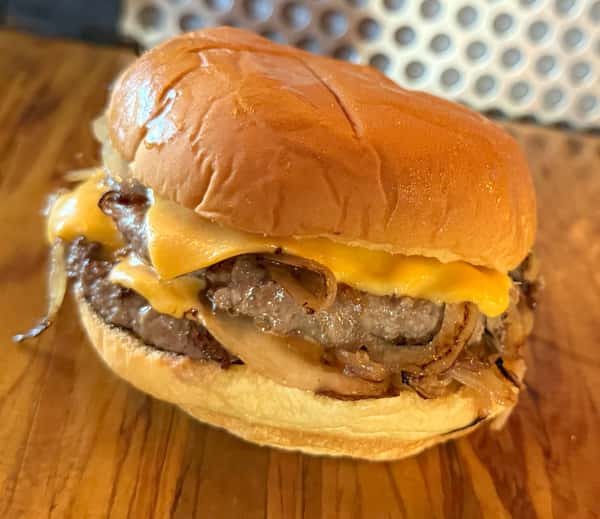 A double cheeseburger with caramelized onions sits on a wooden surface, ready to be enjoyed at Main Street Eats.