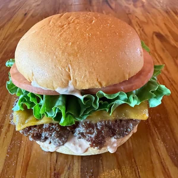A double cheeseburger with lettuce and tomato sits on a wooden table at Main Street Eats.