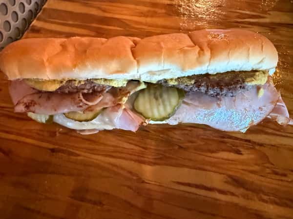 A fully loaded sandwich with ham, pickles, and mustard sits on a wooden surface, ready to be served at Main Street Eats.