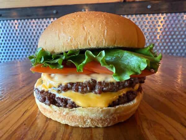 A double cheeseburger with lettuce and tomato sits on a wooden table at Main Street Eats.