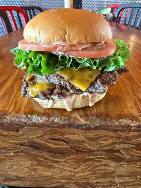 A double cheeseburger topped with lettuce and tomato sits on a wooden table at Main Street Eats.