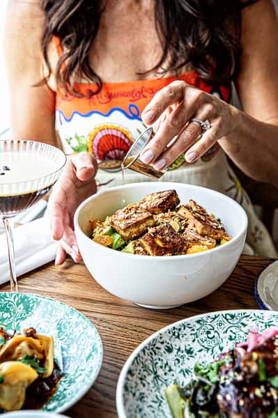 Hand pouring sauce into a bowl of food